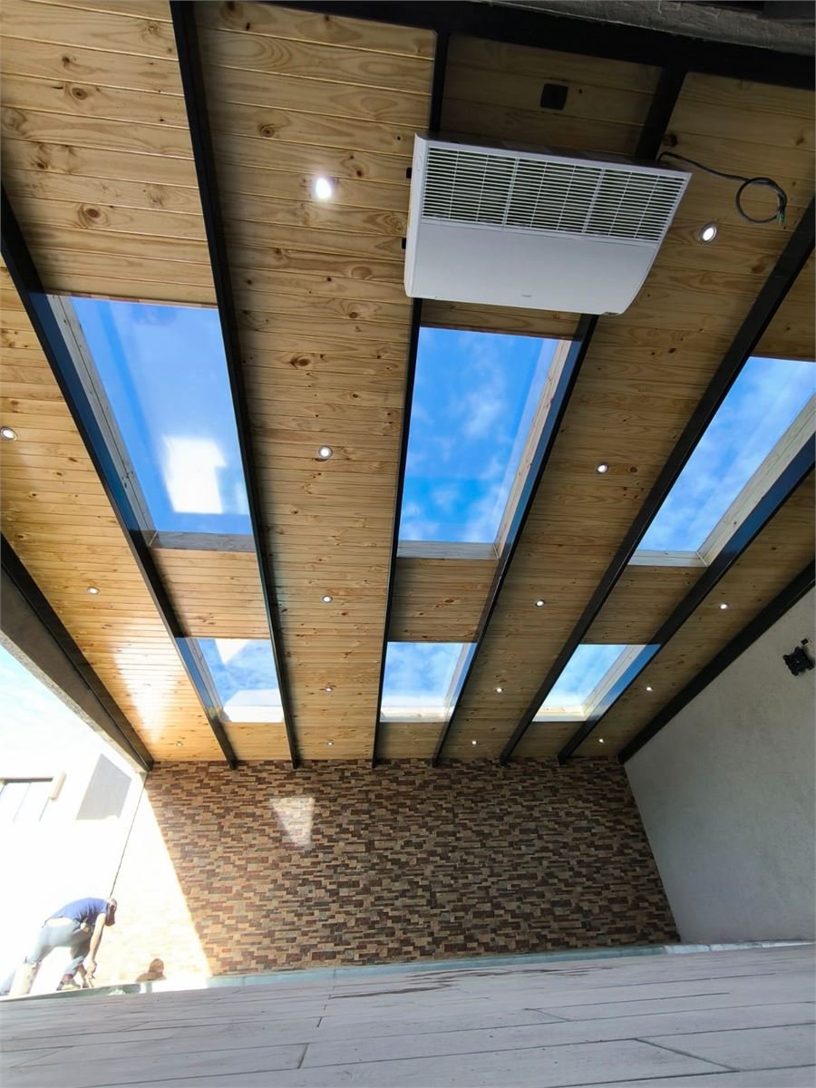 Detalle de vigas metálicas negras y cielo de madera con lucernarios